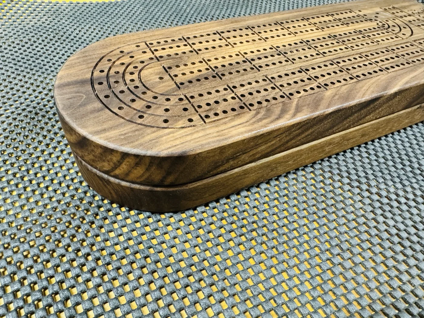 Close view of the cribbage board scoring tracks, curved end, and wooden edge